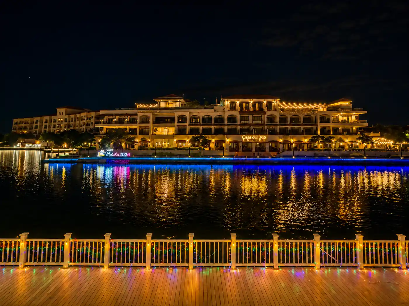 The Melaka River at night with string lights, painted shophouses and a river cruise boat on still water